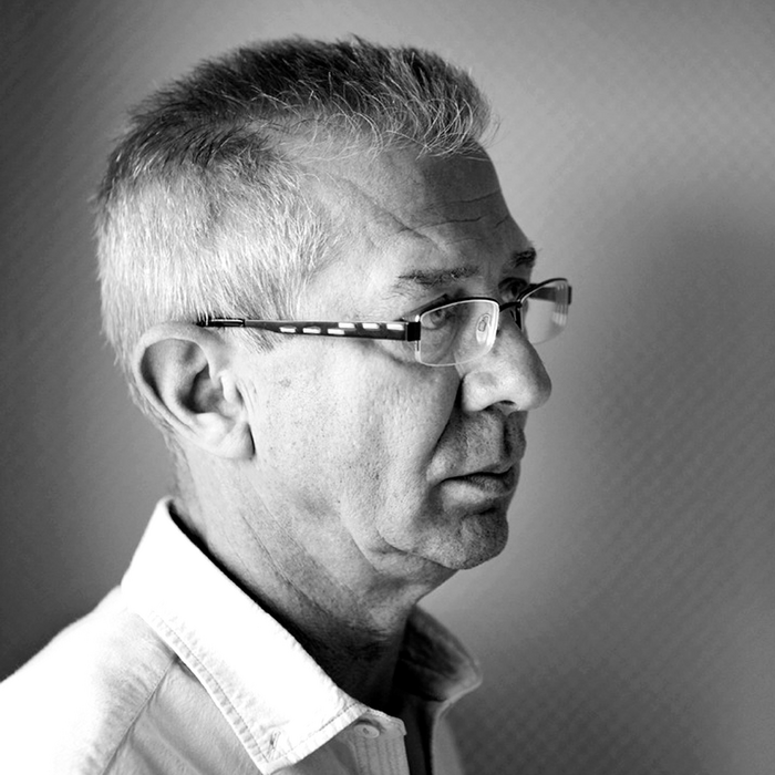 Schwarz-Weiß Porträt eines Mannes mittleren Alters. Er trägt eine Brille und ein weißes Hemd. Sein Blick ist nach rechts gerichtet, was einen nachdenklichen oder konzentrierten Eindruck vermittelt. Kurzes, graues Haar. Das Bild ist scharf fokussiert und betont die Gesichtszüge des Mannes.