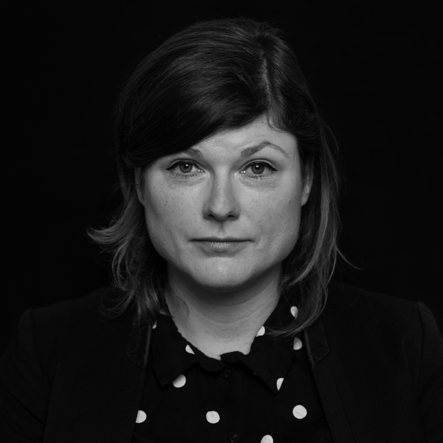 Schwarz-Weiß Porträt einer Frau. Sie hat dunkles, gewelltes Haar und blickt direkt in die Kamera. Ihr Gesichtsausdruck wirkt ernst und nachdenklich. Sie trägt ein dunkles Oberteil mit weißen Punkten.