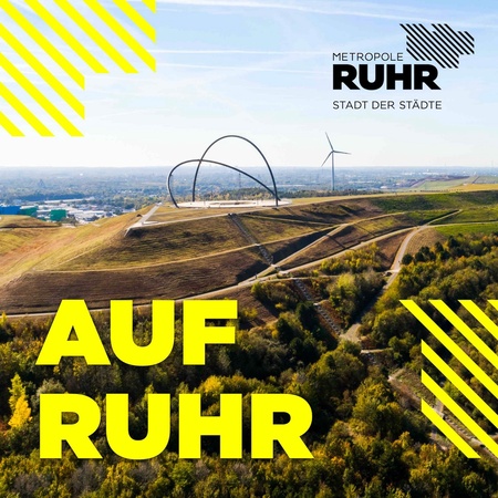 Das Bild zeigt eine weitläufige Landschaft mit einem großen, künstlich angelegten Hügel im Vordergrund. Auf der Hügelspitze befindet sich eine große, kreisförmige Stahlkonstruktion. Im Hintergrund erstreckt sich eine Stadtlandschaft unter einem hellblauen Himmel. Ein Windrad ist ebenfalls zu sehen. Im unteren Bildbereich steht in großen gelben Buchstaben "AUF RUHR". Das Logo "METROPOLE RUHR STADT DER STÄDTE" befindet sich in der oberen rechten Ecke des Bildes. Das Gesamtbild vermittelt einen Eindruck von moderner Architektur und urbanem Raum in einer grünen Umgebung.