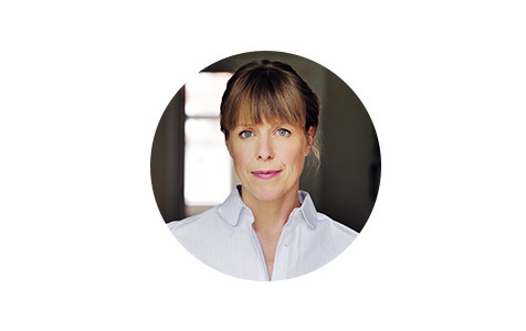 Porträt einer Frau mit kurzen, blonden Haaren. Sie lächelt freundlich in die Kamera und wirkt sympathisch und offen. Der Hintergrund ist neutral weiß.