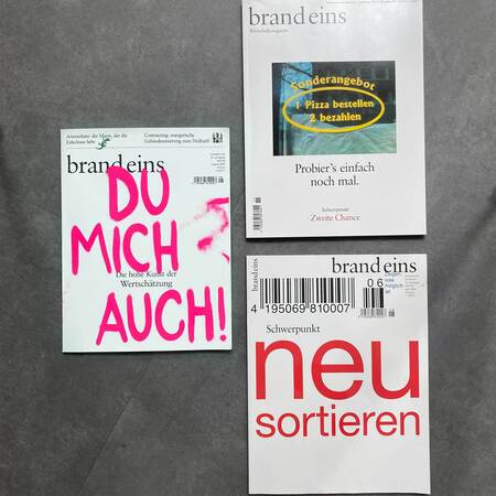 Das Bild zeigt eine Ansammlung von Magazinen der Zeitschrift "brand eins". Im Vordergrund liegt ein Magazin mit dem Titel "neu sortieren" in auffälligen roten Buchstaben. Daneben ein Magazin mit dem Titel "DU MICH AUCH!" in grünen und violetten Buchstaben. Weiter rechts ein Magazin mit einem Sonderangebot für Pizza ("1 Pizza bestellen, 2 bezahlen"). Im Hintergrund sind weitere Magazine zu sehen, darunter eines mit dem Titel "Schwerpunkt Zweite Chance". Die Magazine sind auf einem hellen Untergrund platziert.