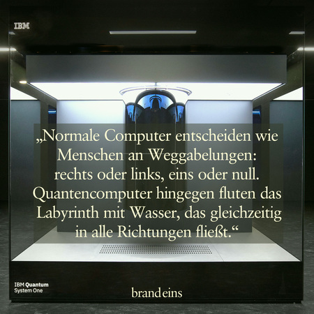 Das Bild zeigt einen dunklen Raum mit einer futuristischen Installation. Im Zentrum steht ein komplexes, metallenes Gerät, das an eine Art Quantencomputer erinnert. Über dem Gerät befindet sich ein Zitat auf hellem Hintergrund: „Normale Computer entscheiden wie Menschen an Weggabelungen: rechts oder links, eins oder null. Quantencomputer hingegen fluten das Labyrinth mit Wasser, das gleichzeitig in alle Richtungen fließt.“ Das Bild vermittelt einen Eindruck von Technologie, Innovation und Komplexität.