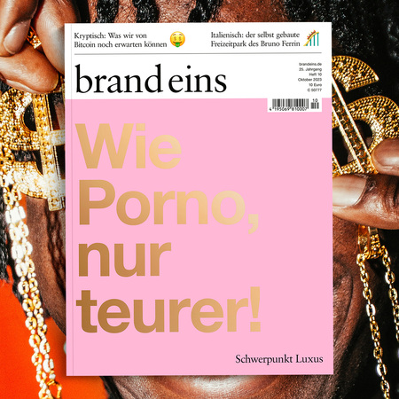 Titelseite des Magazins "brand eins" mit dem Titel "Wie Porno nur teurer". Eine Frau mit dunklen, lockigen Haaren und auffälligem Make-up ist auf der rechten Seite des Bildes zu sehen. Sie trägt ein goldenes Outfit und blickt selbstbewusst in die Kamera. Der Hintergrund ist dunkel, was die Frau hervorhebt. Die Zeitschrift thematisiert Kryptowährungen und Luxus.