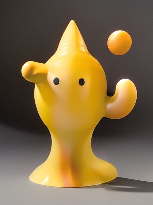 Das Bild zeigt eine gelbe, abstrakte Skulptur, die an eine stilisierte Figur erinnert. Sie hat eine spitze Kopfbedeckung und zwei kleine, runde Augen. Rechts neben der Figur schwebt eine kleinere gelbe Kugel. Die Skulptur wirkt freundlich und verspielt.