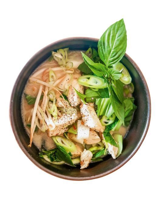 Nahaufnahme einer Schüssel mit Pho, einer vietnamesischen Nudelsuppe. Die Brühe ist hell und cremig, darin befinden sich Reisnudeln, Hühnerfleisch, Frühlingszwiebeln und Kräuter wie Basilikum. Die Suppe wirkt frisch und einladend.