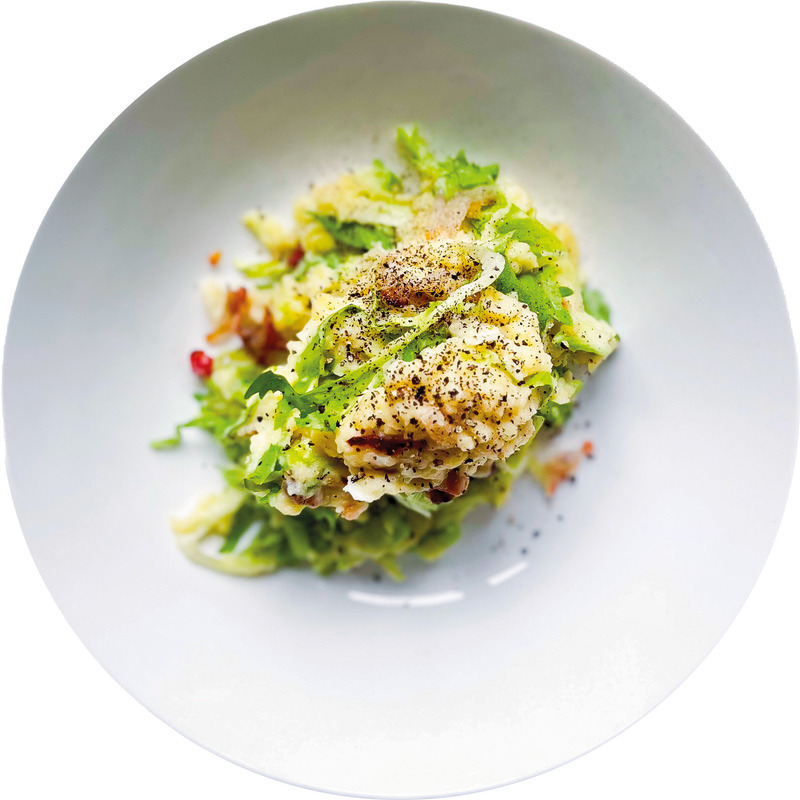 Ein Teller mit einem Gericht aus grünen Blattsalaten, Kartoffeln und einem gebratenen Ei. Das Ei ist in der Mitte des Tellers platziert und mit Pfeffer bestreut. Das Gericht wirkt frisch und appetitlich.