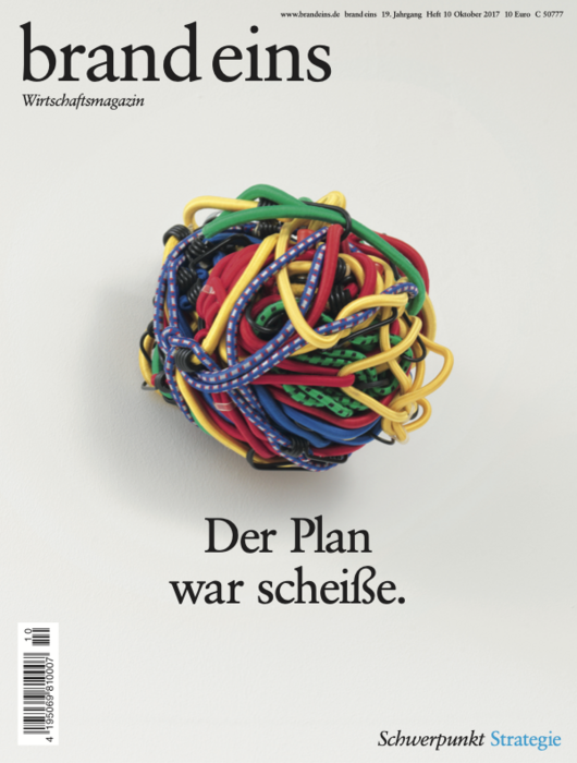 Titelseite eines Wirtschaftsmagazins. Im Zentrum ein großer, unordentlicher Knoten aus bunten Kabeln und Gummibändern auf einem hellgrauen Hintergrund. Darunter in großer Schrift: "Der Plan war scheiße.". Das Magazin trägt den Titel "brand eins" und das Unterthema "Schwerpunkt Strategie".