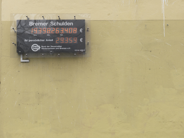 Ein digitales Display an einer beigen Wand zeigt die aktuellen Bremer Schulden in Höhe von 19.398.263.408 Euro an. Darunter wird der persönliche Anteil mit 29.359 Euro ausgewiesen. Das Display wird vom "Bund der Steuerzahler Niedersachsen und Bremen e.V." betrieben.