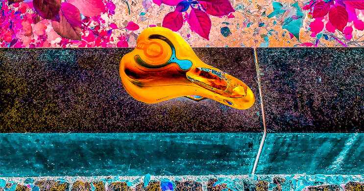Abstraktes Bild mit einem orangefarbenen, spiralförmigen Objekt, das über einem dunklen Wasserverlauf zu schweben scheint. Im Hintergrund sind florale Muster in Pink- und Lilatönen zu erkennen. Das Bild wirkt dynamisch und verspielt.