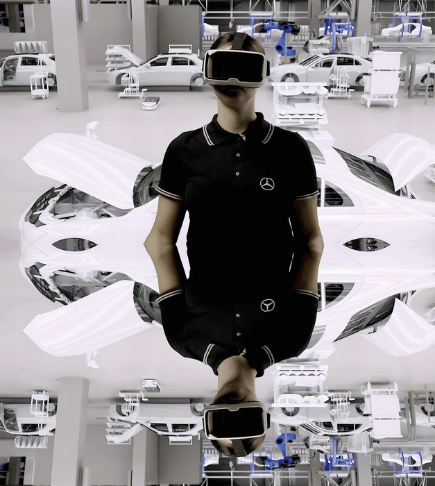 Eine Person mit dunklem Polo-Shirt und schwarzer Hose steht in einem hellen Raum, umgeben von vielen weißen Auto-Modellen. Die Person trägt eine VR-Brille und wirkt konzentriert und in eine virtuelle Welt versunken. Die Hände sind in den Hosentaschen. Das Bild vermittelt einen futuristischen Eindruck von Design und Technologie.