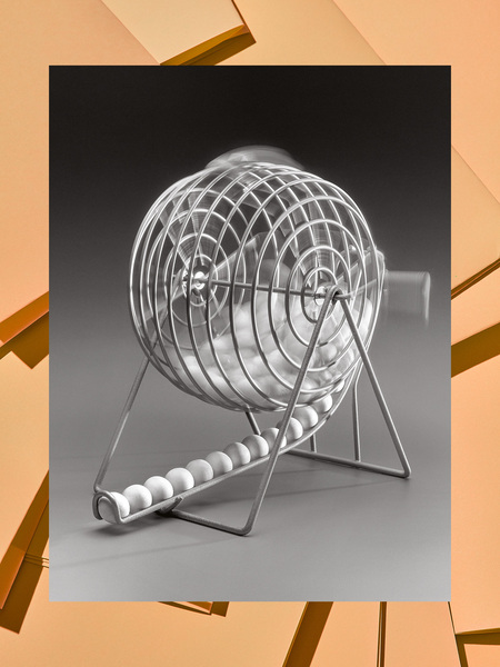 Ein metallischer Bingowürfel mit weißen Kugeln darin steht im Fokus. Das Bild ist in Grautönen gehalten und wird von goldenen, geometrischen Formen umrahmt.