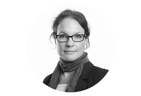 Schwarz-Weiß Porträt einer Frau mittleren Alters mit Brille. Sie trägt einen Blazer und einen Schal. Ihr Blick ist freundlich und wirkt bestimmt.