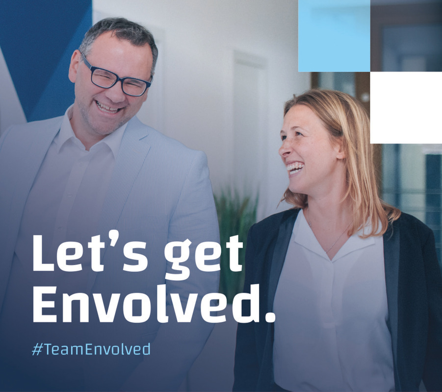 Das Bild zeigt einen Mann und eine Frau, die nahe beieinander stehen, lächeln und sich unterhalten. Sie stehen vor einem blau-weißen Hintergrund, auf dem ein Text mit der Aufschrift "Let's get Involved" eingeblendet ist. Der Text wird von dem Hashtag "#TeamEnthusiast" begleitet, was darauf hinweist, dass das Bild mit einer Social-Media-Kampagne oder -Veranstaltung in Verbindung steht. Das Gesamtlayout und das Design des Bildes scheinen zugänglich und benutzerfreundlich zu sein, so dass es sich für eine Website eignet, die mit den EAA-Richtlinien übereinstimmt.