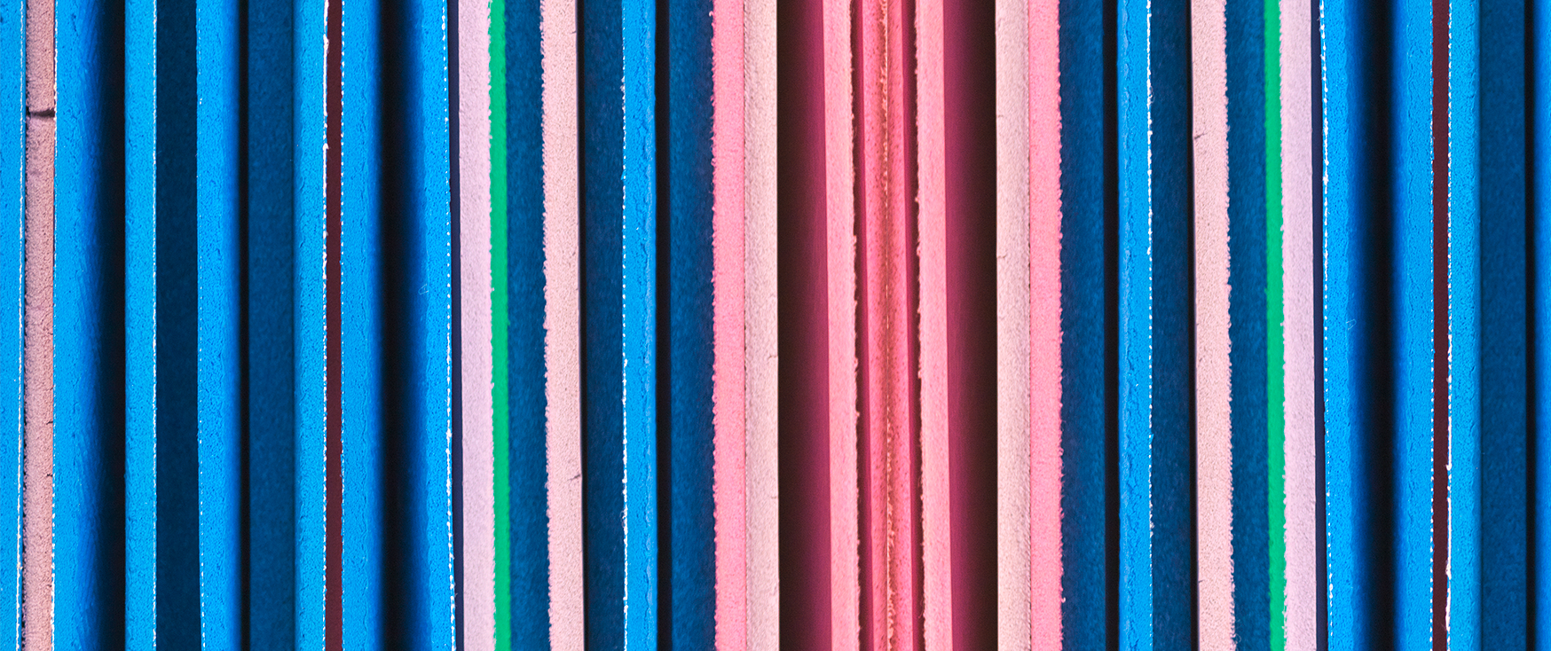 Das Bild zeigt eine Nahaufnahme eines vertikalen Streifenmusters, das aus blauen, rosa und grünen vertikalen Linien besteht. Das Muster setzt sich aus mehreren Reihen vertikaler Linien zusammen, wodurch ein Gefühl von Rhythmus und Bewegung entsteht. Das Bild enthält keinen erkennbaren Text oder zählbare Objekte, und die relativen Positionen der Linien bleiben während des gesamten Musters konstant.