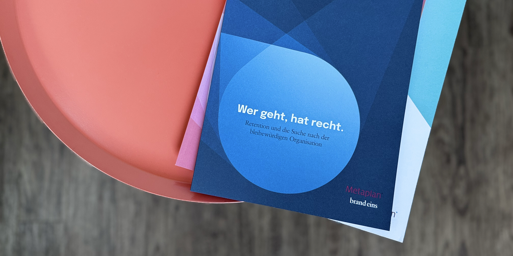 Das Bild zeigt eine Nahaufnahme der Hand einer Person, die eine Broschüre oder einen Flyer in blauer und weißer Farbe hält. Der Text auf der Broschüre ist in deutscher Sprache, und es scheint sich um Werbematerial für ein Unternehmen oder eine Organisation zu handeln. Der Hintergrund des Bildes ist unscharf und lenkt die Aufmerksamkeit des Betrachters auf die Broschüre. Der Text auf der Broschüre lautet "Wer geht, hat recht. Recycling und die suche nach der biodiversity organisation" und "Metaplan brandcins".