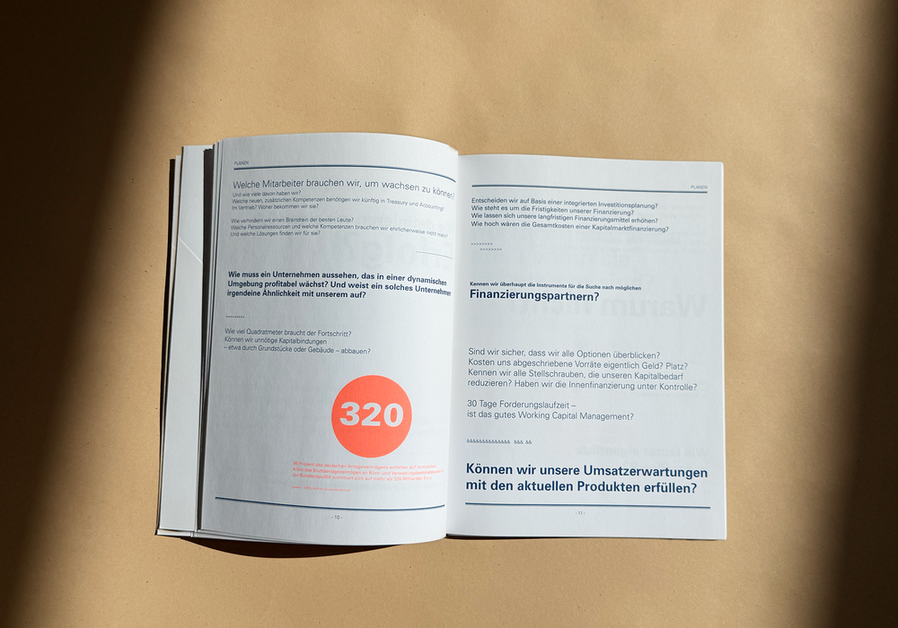 Das Bild zeigt ein aufgeschlagenes Buch mit deutschem Text auf beiden Seiten, das auf einer hölzernen Oberfläche liegt. Bei dem Buch scheint es sich um eine gedruckte Publikation zu handeln, möglicherweise eine Zeitschrift oder ein Buch, mit Schwerpunkt auf Finanz- und Wirtschaftsthemen. Der Text ist in deutscher Sprache, und die Seitenzahlen "320" und "330" sind sichtbar. Das Buch steht vor einem braunen Hintergrund, der den Inhalt hervorhebt und gut lesbar macht.