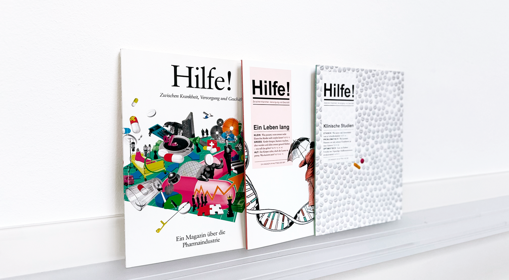 Das Bild zeigt drei Bücher auf einem weißen Regal, jedes mit einem einzigartigen Einbanddesign. Die Bücher tragen die Titel "Hilfe!" und "Hilfe!" in fetten schwarzen Buchstaben, mit zusätzlichem Text in deutscher Sprache. Die Bücher sind in einer Reihe angeordnet, wobei das Buch ganz links eine bunte Illustration verschiedener Objekte aufweist, das mittlere Buch eine detaillierte Illustration einer DNA-Doppelhelix und das Buch ganz rechts einen weißen Hintergrund mit einem Muster aus kleinen Kreisen zeigt. Die Bücher scheinen einen Bezug zum Gesundheitswesen oder zur Medizin zu haben, wie der deutsche Text auf dem Einband vermuten lässt.