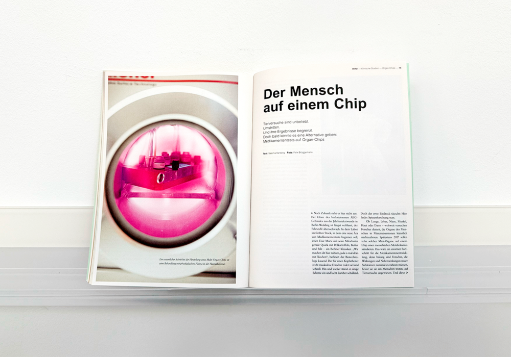 Das Bild zeigt eine aufgeschlagene Zeitschrift oder ein aufgeschlagenes Buch mit einer rosa getönten Fotografie auf der linken Seite und einer Seite mit deutschem Text auf der rechten Seite. Bei der Zeitschrift oder dem Buch scheint es sich um eine Publikation im Zusammenhang mit der Ausstellung "Der Mensch auf einem Chip" zu handeln, die als "Die Erfrischung der kleinen Domestick" und "Die Erfrischung der kleinen Domestick" beschrieben wird. Der Text auf der rechten Seite ist in deutscher Sprache und enthält Informationen über die Ausstellung. Das Layout und die Gestaltung des Magazins oder Buches lassen vermuten, dass es für eine zugängliche Website gedacht ist, die sich an ein vielfältiges Publikum wendet.