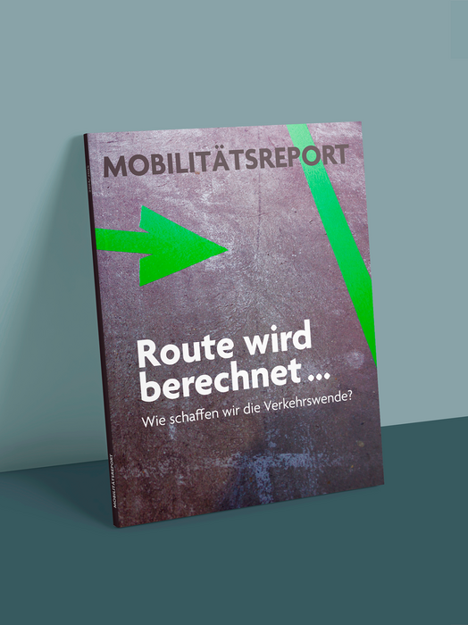 Das Bild zeigt die Titelseite einer Zeitschrift oder Publikation mit dem Titel "MOBILITÄTSREPORT" und einem grünen Pfeil, der nach rechts zeigt. Auf dem Umschlag ist ein Text in deutscher Sprache zu sehen, der lautet "Route wird berechnet..." und "Wie schaffen wir die Verkehrswende?". Der Text ist in den Farben Weiß und Grün gehalten. Der Umschlag steht auf einem blauen Hintergrund, und in der linken unteren Ecke befindet sich ein kleiner Text, der nicht deutlich lesbar ist.