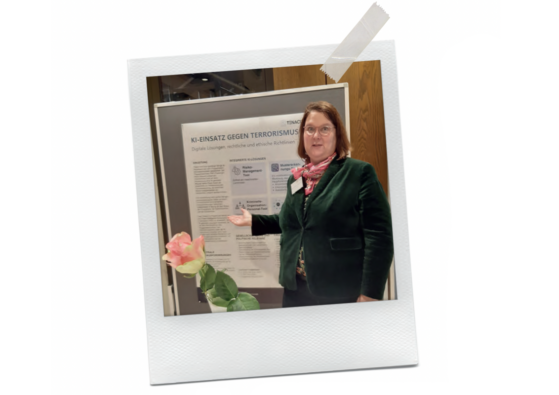 Das Bild zeigt eine Frau, die vor einer Plakatwand steht und eine rosa Rose hält. Sie trägt eine grüne Jacke und ein rotes Halstuch. Die Plakatwand scheint ein Thema zu behandeln, das mit digitaler Sicherheit und Bedrohungen zu tun hat. Die Frau steht vor der Plakatwand und hält die Rose in ihrer Hand.