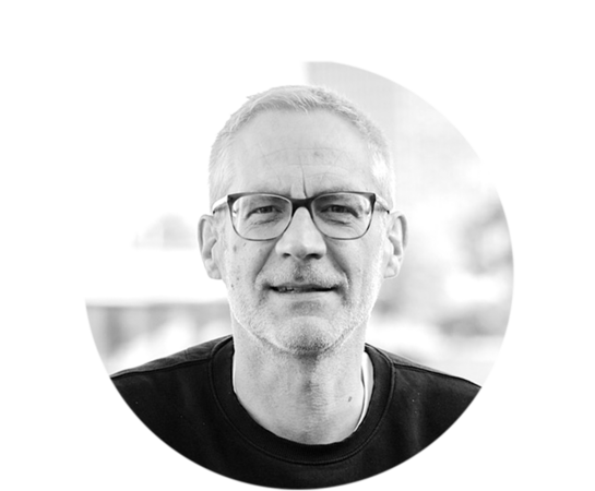 Das Bild ist ein Schwarz-Weiß-Porträt eines Mannes, der eine Brille trägt und einen ernsten Ausdruck im Gesicht hat. Der Mann ist die zentrale Figur im Bild, und der Hintergrund ist unscharf, was die Aufmerksamkeit auf ihn lenkt. Das Bild ist im Hochformat, und der Mann ist das einzige Objekt im Bild. Das Bild enthält keinen Text oder andere erkennbare Objekte.