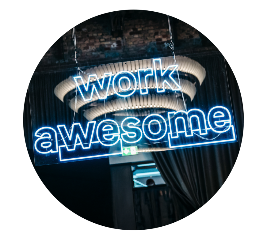 Das Bild zeigt eine Leuchtreklame mit der Aufschrift „work awesome“ in blauen Neonlichtern. Die Leuchtreklame hängt von der Decke herab und sorgt für einen auffälligen visuellen Effekt. Der Hintergrund ist dunkel, wodurch die Leuchtreklame und ihre Botschaft besonders hervorgehoben werden. Die Leuchtreklame scheint Teil einer größeren Ausstellung oder Installation zu sein, möglicherweise in einem Veranstaltungsort oder Veranstaltungsraum. Das Bild enthält keinen erkennbaren Text oder andere Objekte, und die Leuchtreklame steht im Mittelpunkt, wobei der Hintergrund absichtlich unscharf gehalten ist, um die Aufmerksamkeit auf die Botschaft der Leuchtreklame zu lenken.