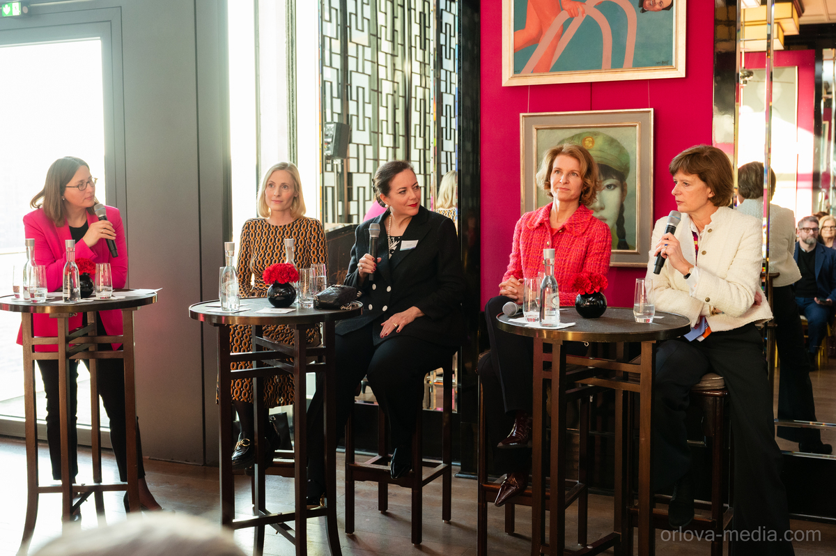 Das Bild zeigt eine Gruppe von fünf Frauen, die an runden Tischen in einem farbenfrohen Raum sitzen und sich an einer Diskussion oder Präsentation beteiligen. Jede Frau hält ein Mikrofon in der Hand, was darauf hindeutet, dass sie an einer formellen Veranstaltung oder Konferenz teilnehmen. Der Raum ist modern und stilvoll eingerichtet, mit einer rosa Wand und einem großen Gemälde an der Wand. Die Frauen sind professionell gekleidet, und auf den Tischen stehen mehrere Flaschen und Tassen, was darauf hindeutet, dass während der Veranstaltung Erfrischungen serviert werden. Das Bild enthält außerdem den Text „oriva-media.com“, was entweder der Name der Website sein könnte, von der das Bild stammt, oder ein Hinweis auf den Veranstalter der Veranstaltung.