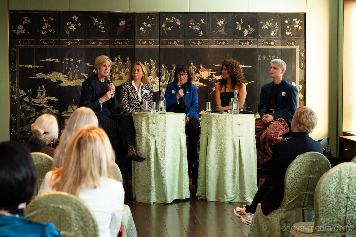 Das Bild zeigt eine Podiumsdiskussion mit fünf Personen, die an einem Tisch sitzen, jeweils ein Mikrofon in der Hand halten und sich unterhalten. Der Rahmen scheint eine formelle Veranstaltung oder Konferenz zu sein, mit einer großen Leinwand oder Wand im Hintergrund, auf der ein kunstvolles Design zu sehen ist. Das Publikum sitzt auf Stühlen und hört den Rednern aufmerksam zu. Das Bild ist im Hochformat und der Text „ofava.media.com” ist sichtbar, was wahrscheinlich auf die Quelle oder Website im Zusammenhang mit der Veranstaltung hinweist.