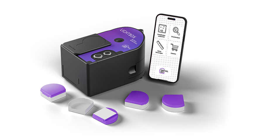 Das Bild zeigt ein violettes und schwarzes Gerät sowie ein Smartphone mit einer weißen Benutzeroberfläche, auf der Symbole und Text zu sehen sind; beides steht auf einer weißen Unterlage. Außerdem sind mehrere violette und weiße Behälter mit Deckeln zu sehen, was auf ein Produkt oder eine Dienstleistung hindeutet, die mit dem Gerät oder dem Smartphone in Zusammenhang steht. Das Bild ist für die EAA zugänglich, da es auf deren Website als Produktbild für ein Produkt beschrieben wird.